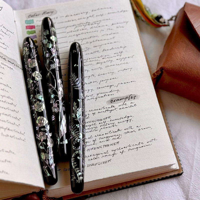 Three CYPRESS × @micahfinds Victorian Flora: The Humble Fern (14K Gold) Fountain Pens On Top Of Notebook | EndlessPens